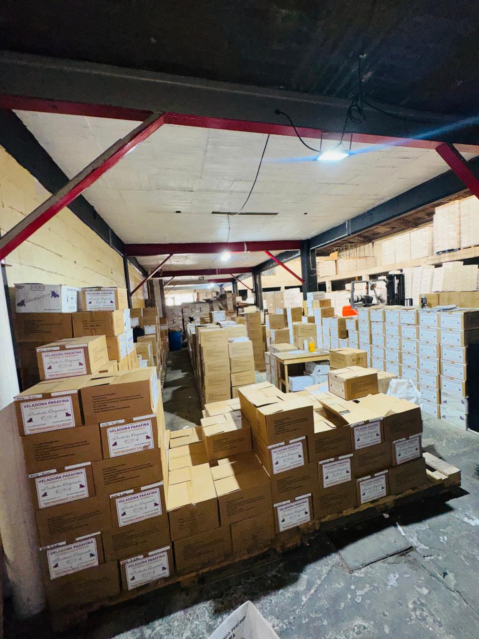 Pasillo de la bodega con cajas apiladas hasta el techo y montacargas al fondo